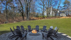 Un foyer circulaire entouré de chaises Adirondack, installé sur une terrasse en pierre.