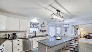 Une cuisine moderne avec des meubles blancs, un grand îlot central doté de tabourets, et un coin repas agrémenté d’un sapin de Noël.