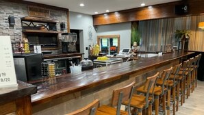 Un espace bar avec des tabourets de bar en bois, un long comptoir et un tableau affichant le menu.