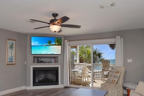 A living room with a television, fireplace, and a view of the ocean through large sliding doors. - Barrier Dunes 156 - 11 Sand Dollar Dreams (Port St. Joe)