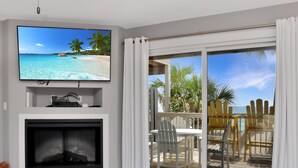 Ein Wohnzimmer mit Fernseher, Kamin und Meerblick durch eine Glasschiebetür.