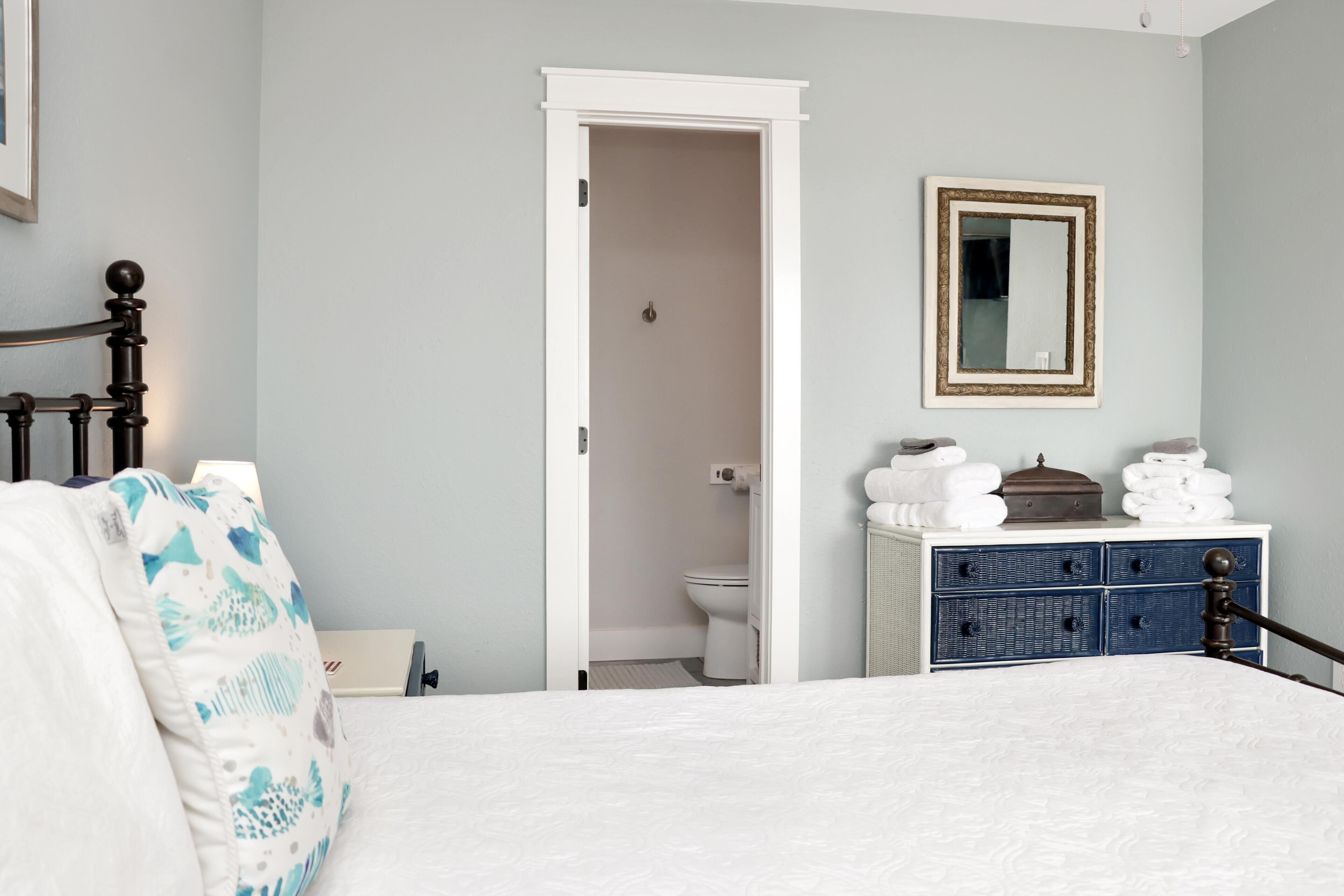 A bedroom with a bed, a dresser, a mirror, and a door leading to a bathroom.