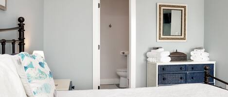 A bedroom with a bed, a dresser, a mirror, and a door leading to a bathroom.