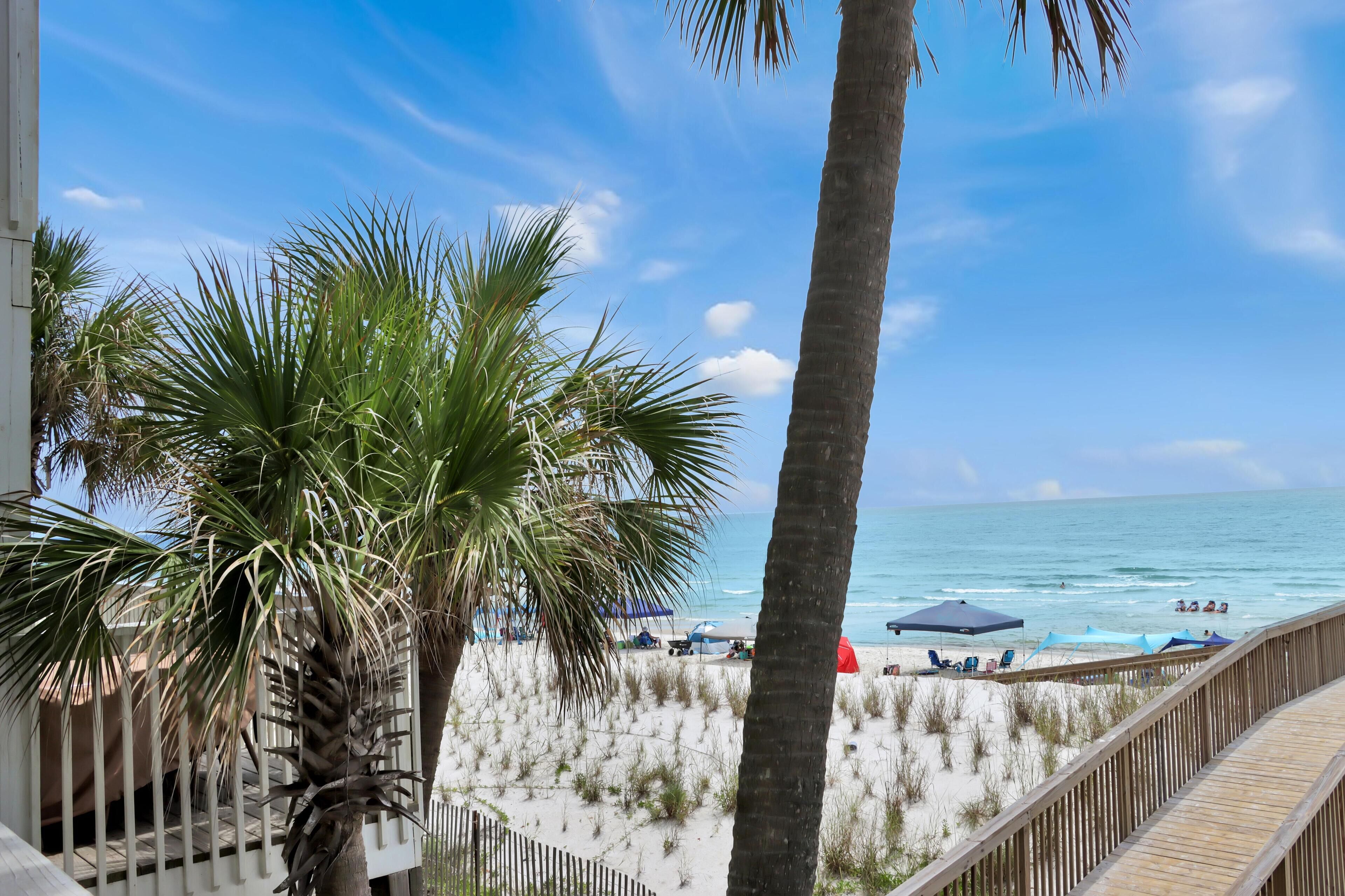 Une vue sur la plage, avec des palmiers, une terrasse en bois et des parasols de plage.