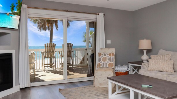 Ein Wohnzimmer mit Fernseher, einer Couch, einem Couchtisch, einer Lampe und Blick auf den Strand durch eine Schiebetür.