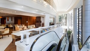 Un vestíbulo moderno de hotel con un amplio espacio de descanso, una escalera central y una barandilla de vidrio que da a un nivel inferior.