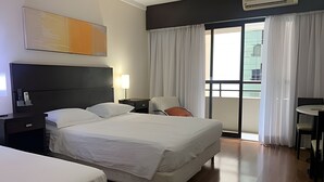 Una habitación de hotel con una cama grande, un escritorio, una silla y un balcón con cortinas.