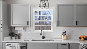 A modern kitchen with grey cabinets, a white countertop, a window with a view of trees, a sink, and a stove. - Spacious 6-bedroom house in beautiful Downtown Brevard (Brevard)