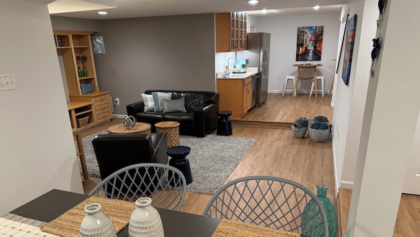 A modern living room with a black leather sofa, a dining table with woven placemats, and a kitchen area in the background. - Clean comfy Reston B&B with ping pong table (Reston)