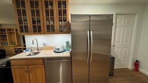 A kitchen with wooden cabinets, a stainless steel refrigerator, a sink, and a countertop with various items. - Clean comfy Reston B&B with ping pong table (Reston)