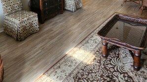 Una sala de estar con un televisor de pantalla plana grande, sillas estampadas, un mueble de madera y una alfombra con motivos.