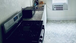 A kitchen with a stove, microwave, and a window with blinds.