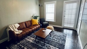 A living room with a brown leather sofa, a wooden coffee table, a patterned rug, and a ceiling light.