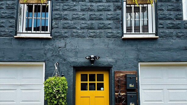 A two-story building with a yellow front door, two garage doors, and a mailbox.