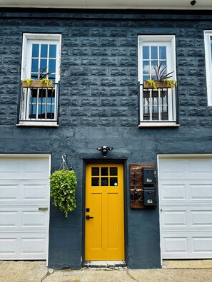 Un bâtiment à deux étages avec une porte d’entrée jaune, deux portes de garage et une boîte aux lettres.