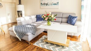 A modern living room with a grey sectional sofa, a white coffee table, and a decorative vase with flowers. - Baltic Village - Ostsee-Villa (Damp)