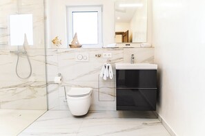 Une salle de bain moderne dotée d’une douche à parois de verre, de toilettes, d’un lavabo avec un meuble noir en dessous et d’un miroir au-dessus du lavabo.