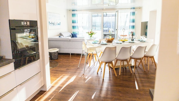 A modern kitchen with a built-in oven and a dining area with a white table and chairs. - Baltic Village - Ostsee-Villa (Damp)