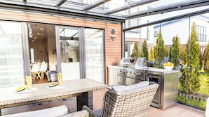 An outdoor patio with a dining table, wicker chairs, and a stainless steel grill. - Baltic Village - Ostsee-Villa (Damp)