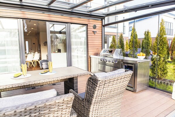 Une terrasse extérieure avec une table à manger, des chaises en osier et un barbecue en acier inoxydable.