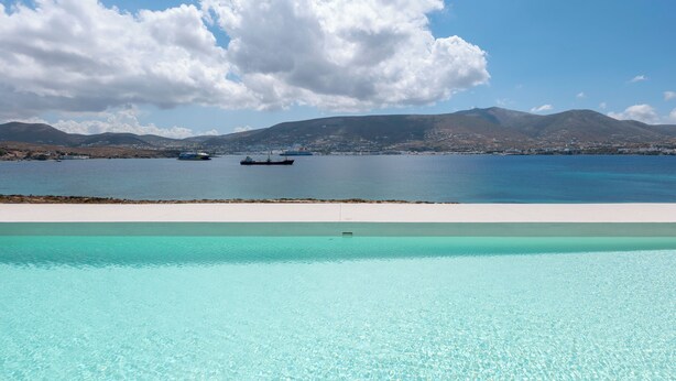 A clear blue pool with a view of a calm sea and distant mountains. - Donum Dei Seaside Suites & Villa (Paros)