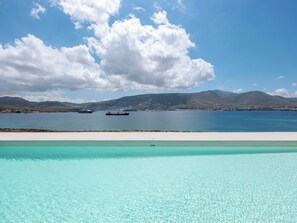 A clear blue pool with a view of a calm sea and distant mountains. - Donum Dei Seaside Suites & Villa (Paros)