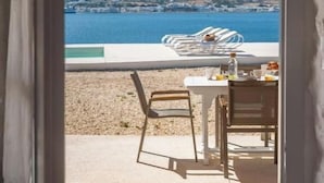 A view from a balcony overlooking a coastal area with a pool and dining setup. - Donum Dei Seaside Suites & Villa (Paros)