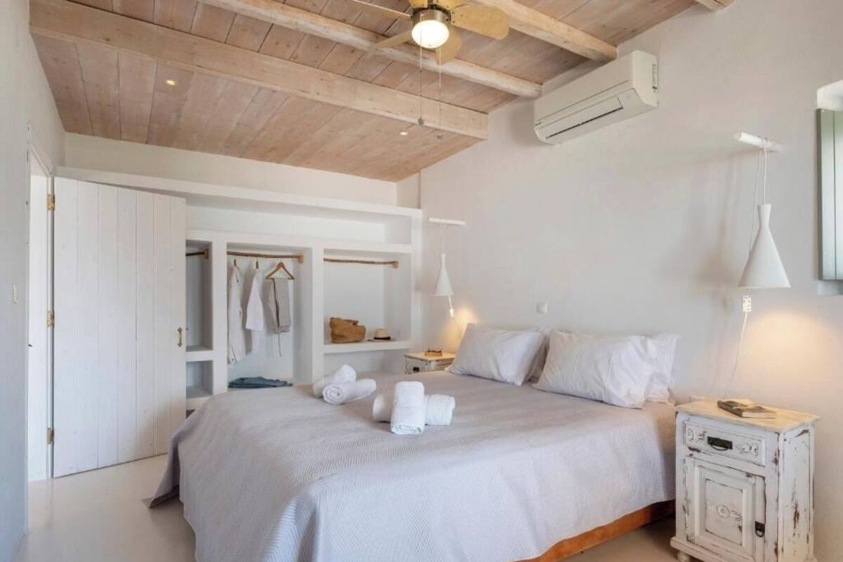 Quarto com cama grande, guarda-roupa, mesa de cabeceira e ventoinha no teto.