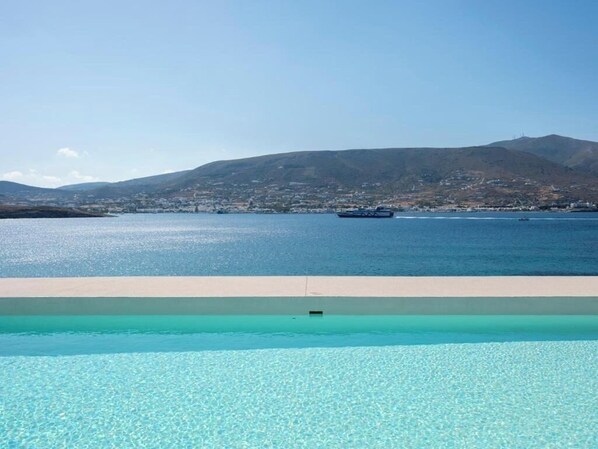 A pool with clear water and a view of a body of water and distant land. - Donum Dei Seaside Suites & Villa (Paros)
