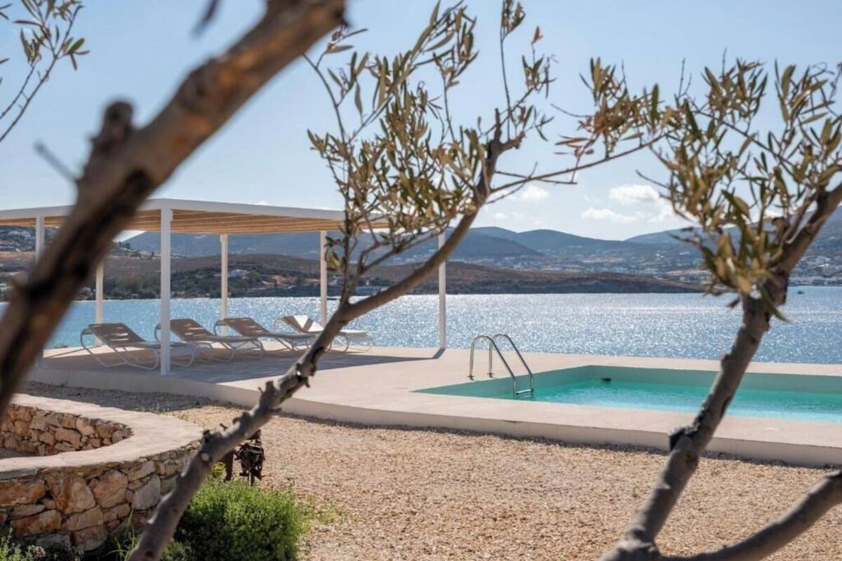 Área de piscina com espreguiçadeiras e um pérgola com vista para um corpo de água.