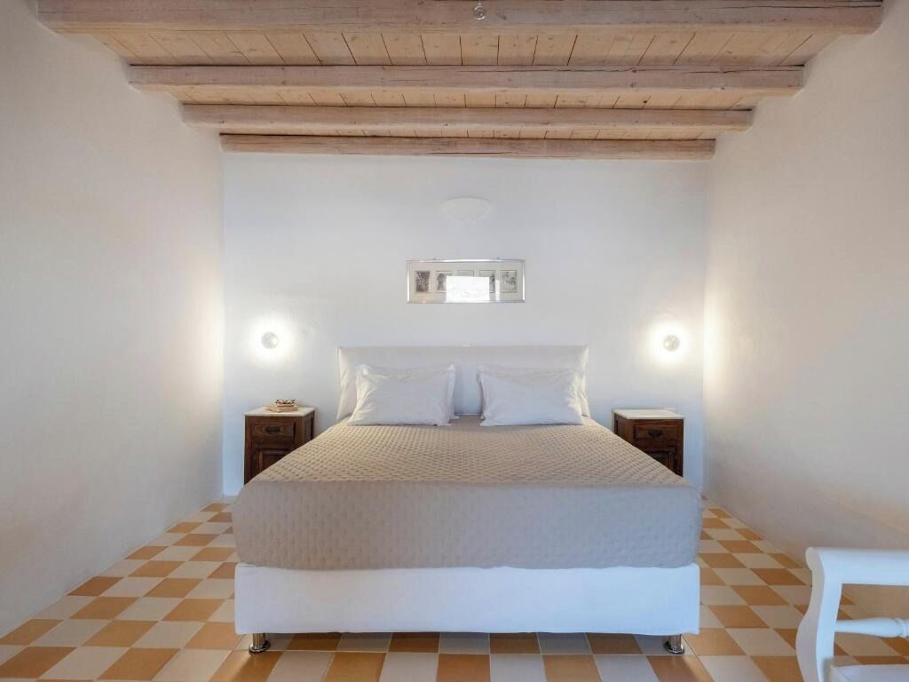 A bedroom with a large bed, two bedside tables, a small bedside lamp, and a checkered floor.