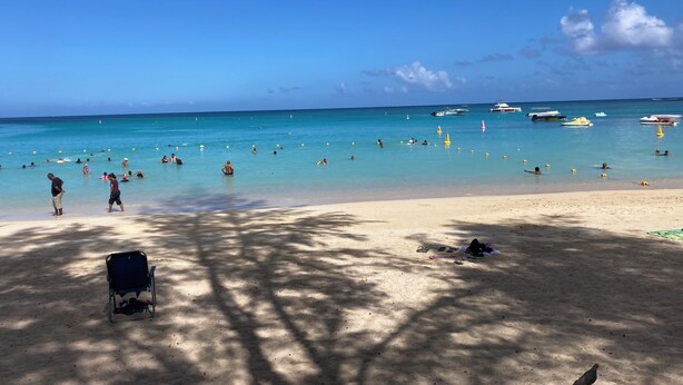 A beach with clear blue water, people swimming and sunbathing, and boats in the distance. - Space Villa 3 (Grand Baie)