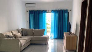 A living room with a beige sectional sofa, a wooden cabinet, and a television on a stand. - Space Villa 3 (Grand Baie)