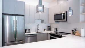 Une cuisine moderne dotée d’appareils électroménagers en acier inoxydable, de meubles blancs et d’un éclairage suspendu.