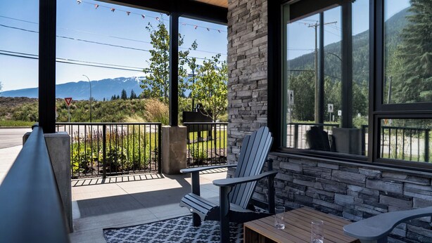 Une terrasse couverte, dotée de fauteuils Adirondack, d’une table en bois et offrant une vue sur un paysage montagneux.