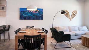 Un espace repas moderne avec une table en bois, des chaises noires et un luminaire suspendu blanc.