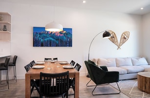 Un comedor moderno con una mesa de madera, sillas negras y una lámpara colgante blanca.