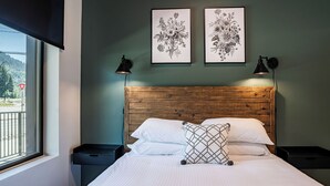 Une chambre avec une tête de lit en bois, deux tables de chevet, un lit avec une literie blanche, deux lampes fixées au mur et deux reproductions botaniques encadrées.