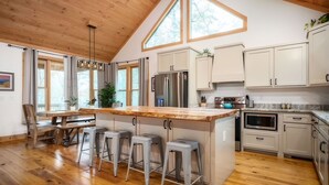 A modern kitchen with wooden flooring, a large island with bar stools, white cabinets, and a stainless steel refrigerator. - McStay in McCay - Charming 4-bed cabin w/ outdoor fireplace and large jacuzzi!  (McCaysville)