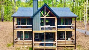 A multi-story cabin with a central chimney, wooden balconies, and large windows. - McStay in McCay - Charming 4-bed cabin w/ outdoor fireplace and large jacuzzi!  (McCaysville)