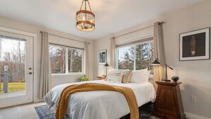 A bedroom with a bed, a wooden nightstand, a floor lamp, and a window with curtains. - Set & Drift | Hatcher Pass, Pets Allowed, Peaceful (Palmer)