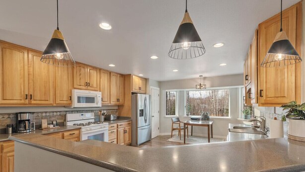 A modern kitchen with wooden cabinets, stainless steel appliances, and pendant lighting. - Set & Drift | Hatcher Pass, Pets Allowed, Peaceful (Palmer)