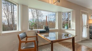 A room with a large glass table, two chairs, and a view of trees through large windows. - Set & Drift | Hatcher Pass, Pets Allowed, Peaceful (Palmer)