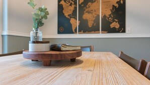A wooden dining table with a glass vase containing green foliage, a white bowl, and a book on a wooden coaster. A world map is displayed on the wall behind. - Set & Drift | Hatcher Pass, Pets Allowed, Peaceful (Palmer)