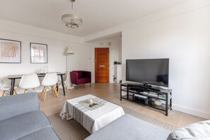 Ein modernes Wohnzimmer mit Flachbildfernseher, einem Essbereich mit Tisch und Stühlen sowie einem roten Sessel.