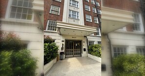 A building entrance with a double door, a small garden area, and a pathway leading to the entrance.