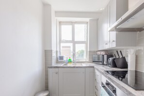 A modern kitchen with a built-in stove, microwave, and a window with a view of buildings. - Cosy 1BD Flat 5 Minutes from Hyde Park (London)