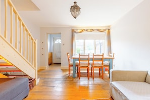 A spacious living room with a wooden staircase, a dining area with a table and chairs, and a cozy seating area with a sofa. - Charming 2BD Canal-Side Home in East London (London)