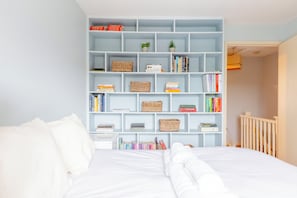 A bedroom with a large bed, a white headboard, and a light blue bookshelf filled with books and decorative items. - Charming 2BD Canal-Side Home in East London (London)
