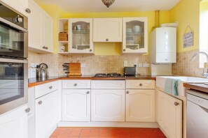 A kitchen with white cabinets, a gas stove, a kettle, and a sink. - Charming 2BD Canal-Side Home in East London (London)